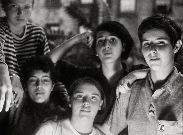 A black and white photo of a group of young queer women sat together looking toward the camera.